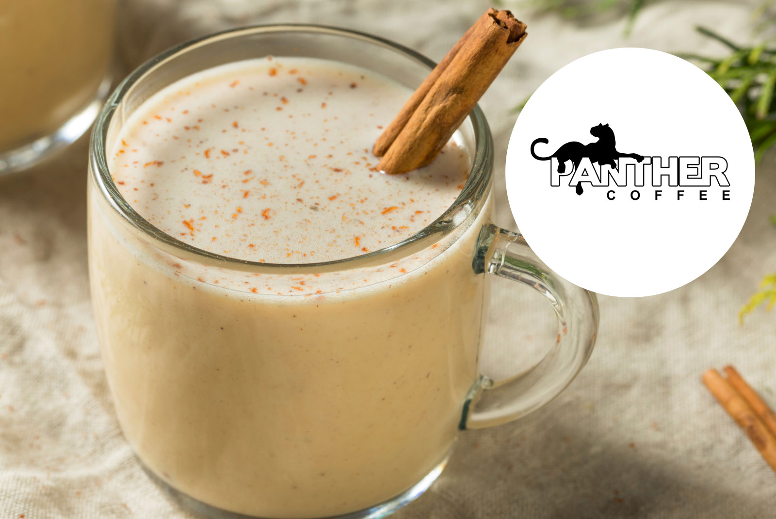 A glass mug of creamy Coquito, topped with ground spice and a cinnamon stick, sits on a light surface. The Miami Panther Coffee logo appears in a white circle on the right side of the image.