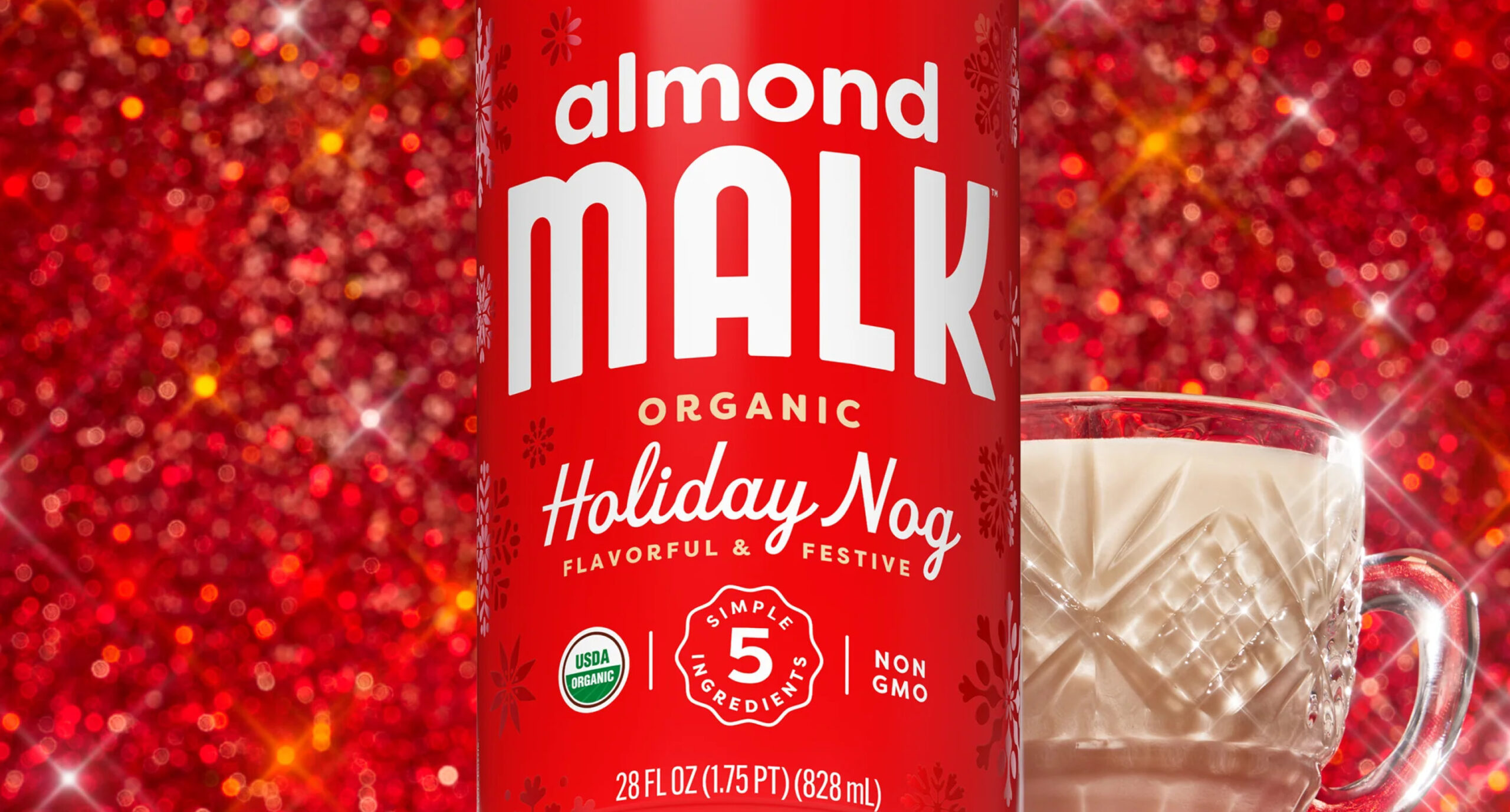 A red carton of Almond Malk Organic Holiday Nog, part of our New Arrivals, stands before a sparkling red background, with a glass of the creamy beverage beside it. The carton features festive snowflake designs and holiday-themed text.