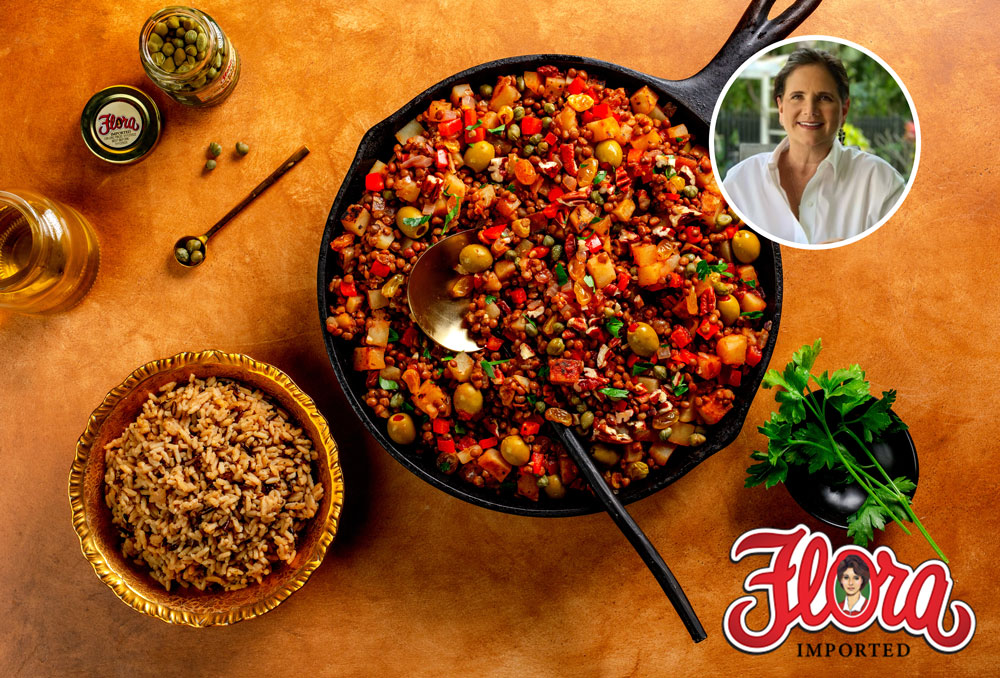 A skillet of Cuban Style picadillo with olives and vegetables sits on a brown surface next to a bowl of rice. Fresh herbs, capers, olive oil, and a Flora logo appear. An inset shows a smiling woman in white.