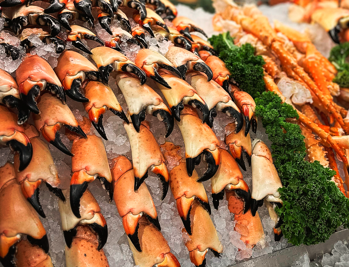 A display of fresh crab claws arranged on ice with leafy green garnish beside them, showcasing prime fresh seafood at a market or restaurant.